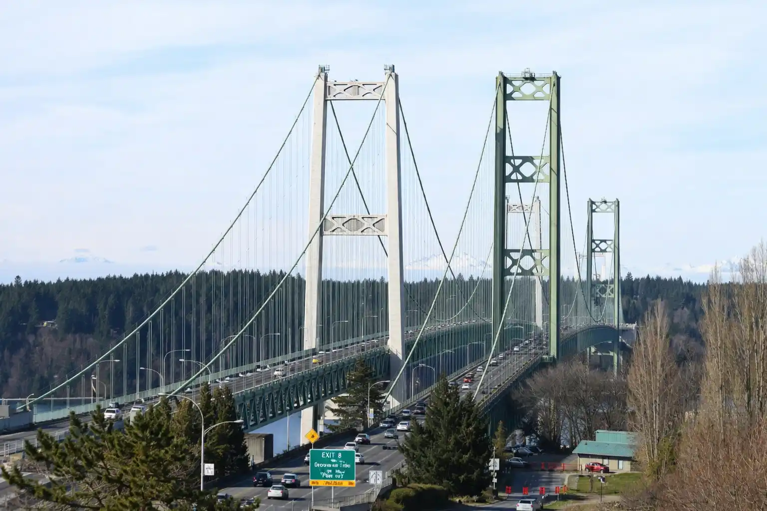 Black luxury sedan crossing Tacoma Narrows Bridge toward Gig Harbor on overcast Pacific Northwest day, professional corporate transportation