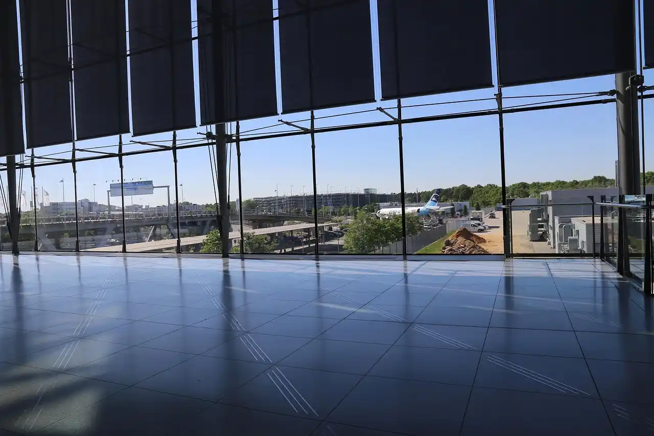 professional chauffeur in a black suit holding a name sign inside SeaTac airport arrivals hall with travelers walking by and large glass windows