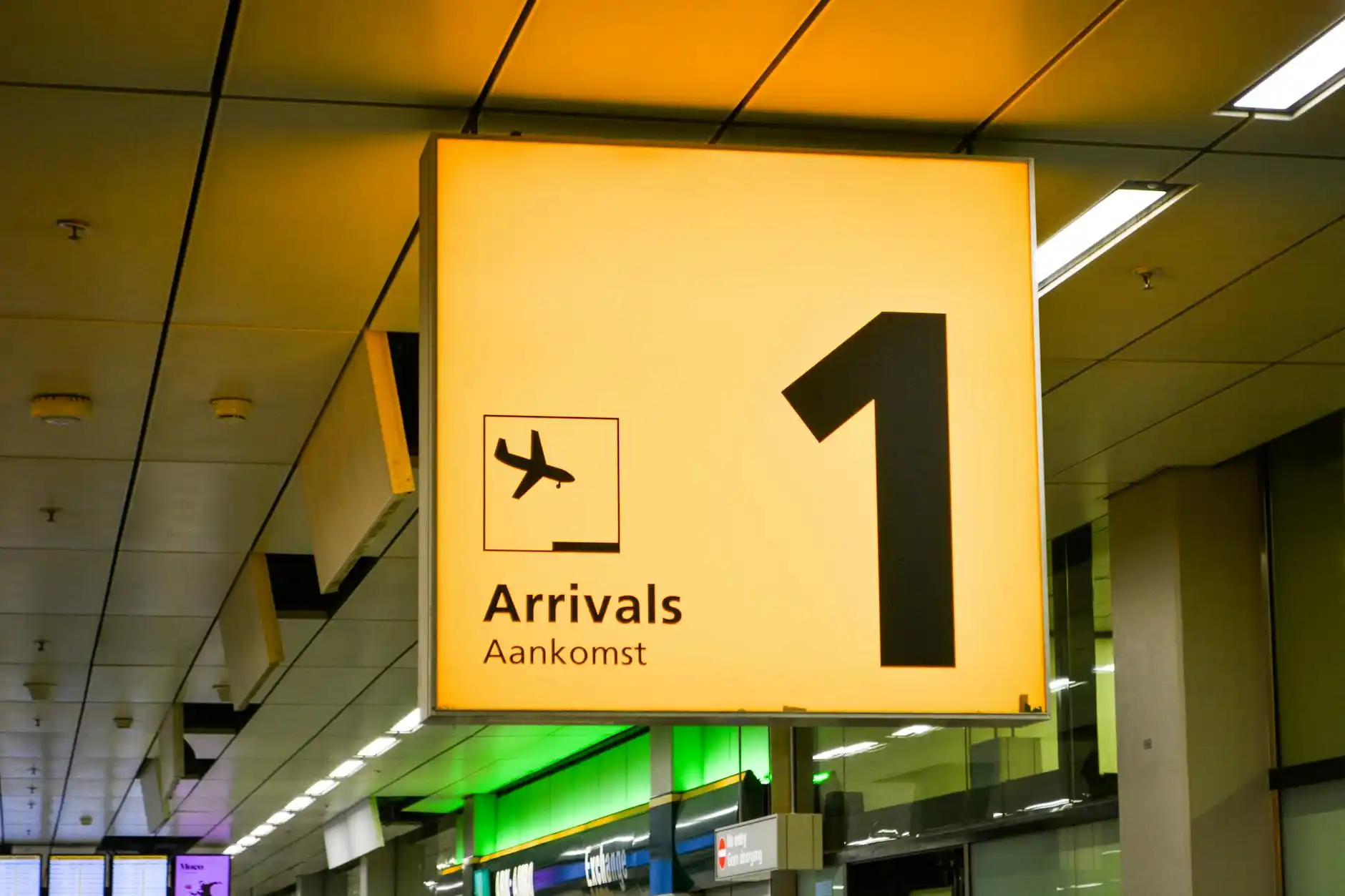 busy baggage claim area at SeaTac with luggage carousel, travelers collecting bags, and chauffeur holding a name sign nearby