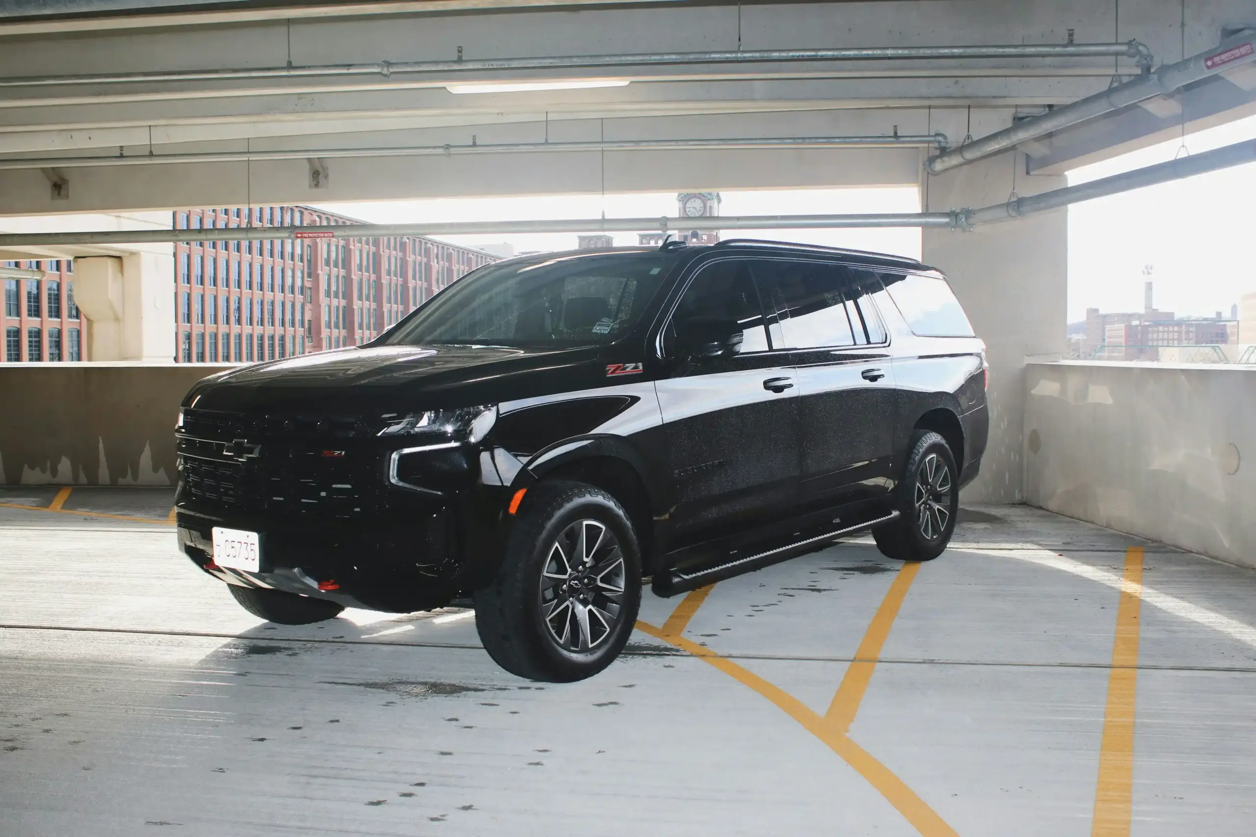 black luxury SUV waiting near Anacortes Ferry Terminal at golden hour, ferry unloading in background, travelers with rolling luggage approaching curbside pickup