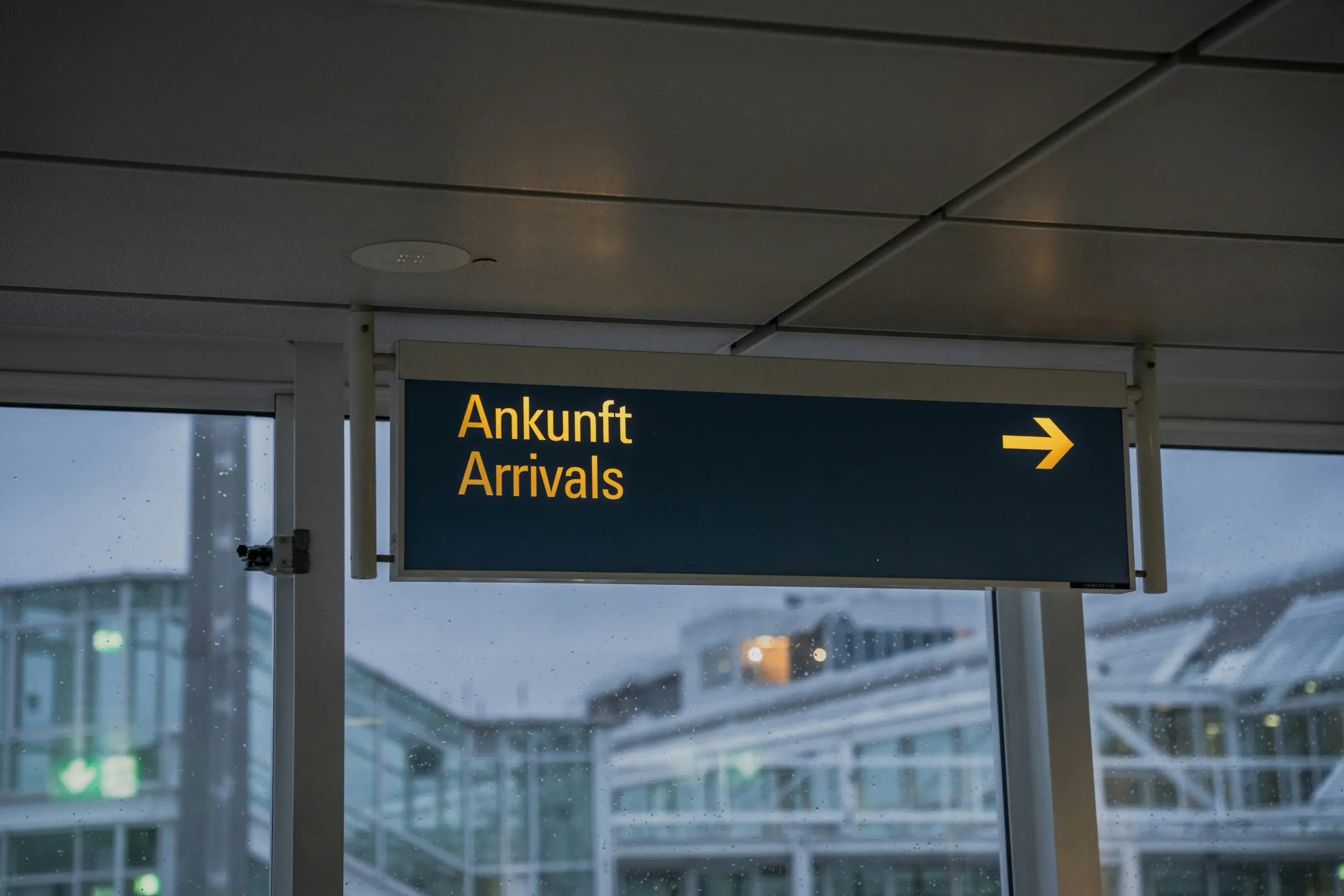 professional chauffeur in a dark suit holding a personalized name sign inside Seattle-Tacoma International Airport arrivals hall, travelers walking past, bright terminal lightin...