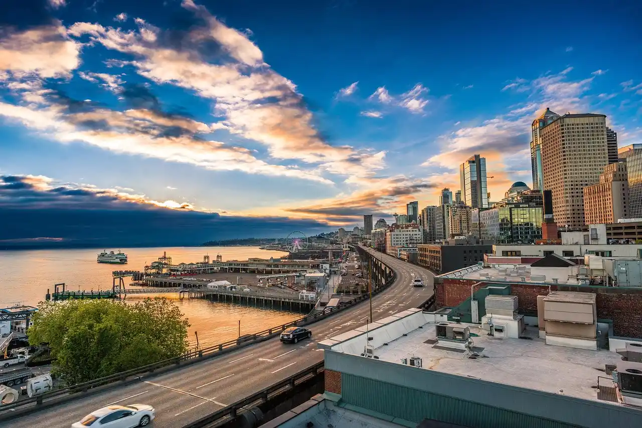 lineup of luxury vehicles including sedan SUV and sprinter van parked in front of a modern Seattle skyline backdrop at sunset