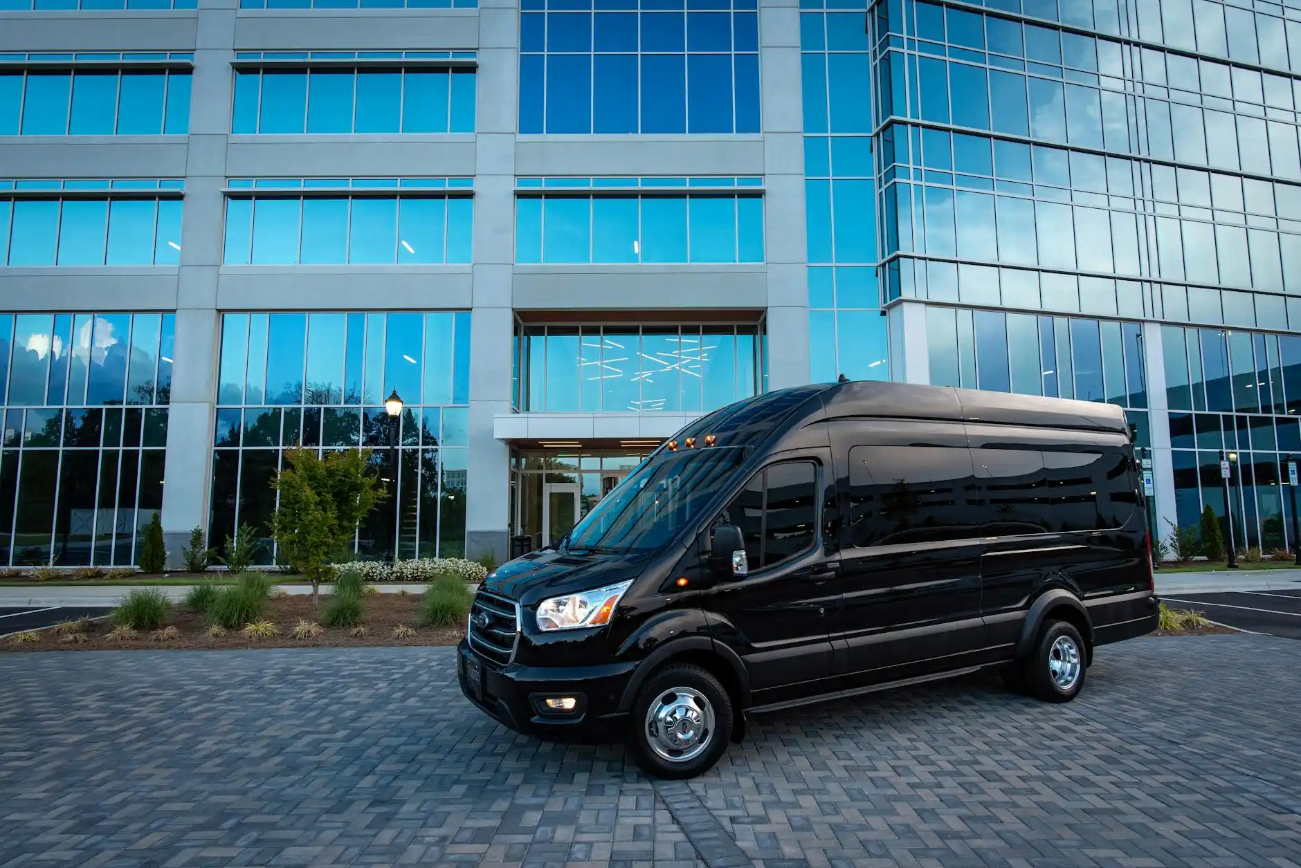 black Mercedes Sprinter van parked near Seattle downtown high-rise hotel entrance on a clear morning, chauffeur loading suitcases, urban skyline and glass towers in background