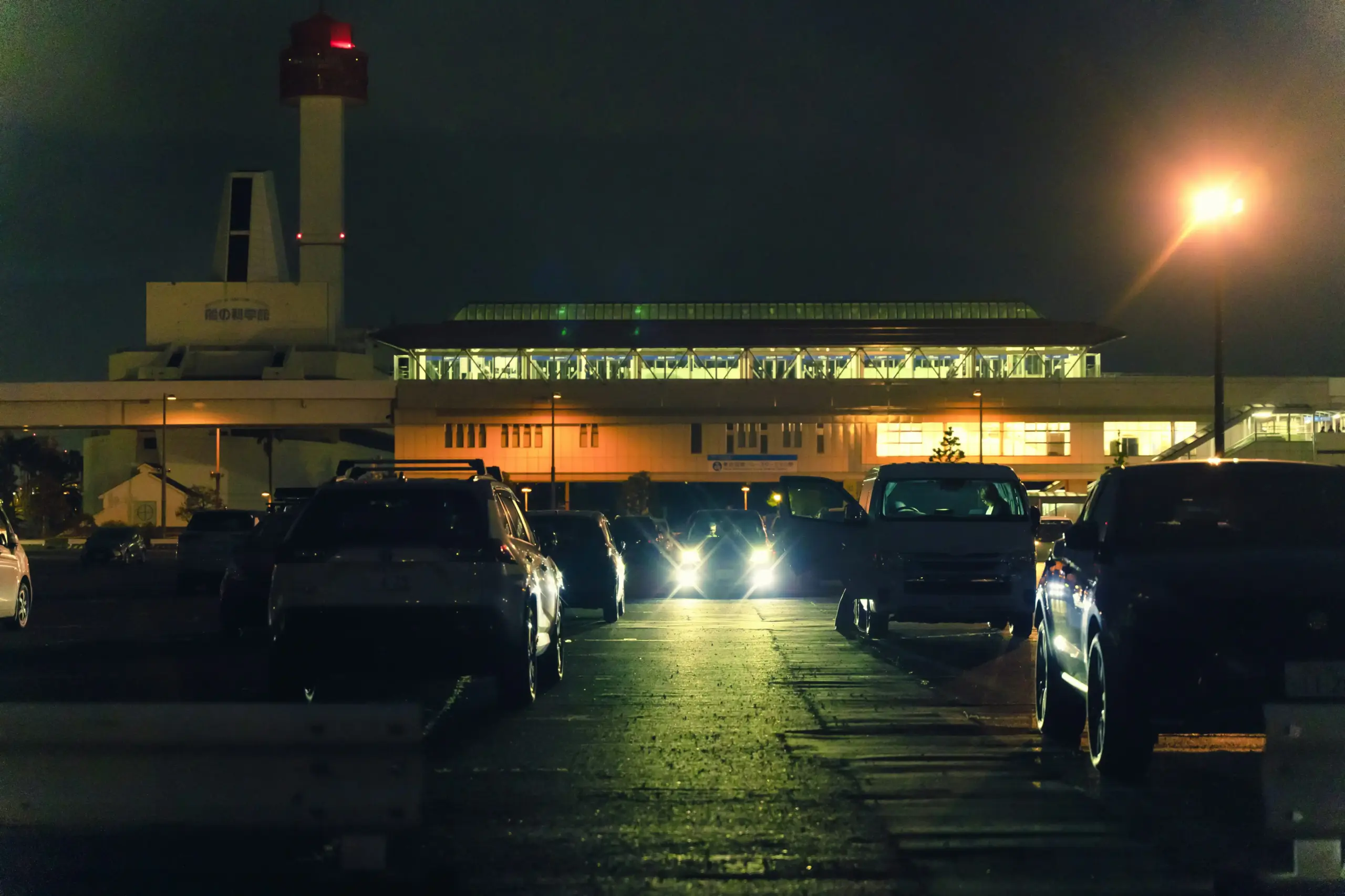 black luxury SUV parked at Vancouver International Airport arrivals curb at dusk, driver in dark suit holding digital name sign, wet pavement reflecting terminal lights, travele...