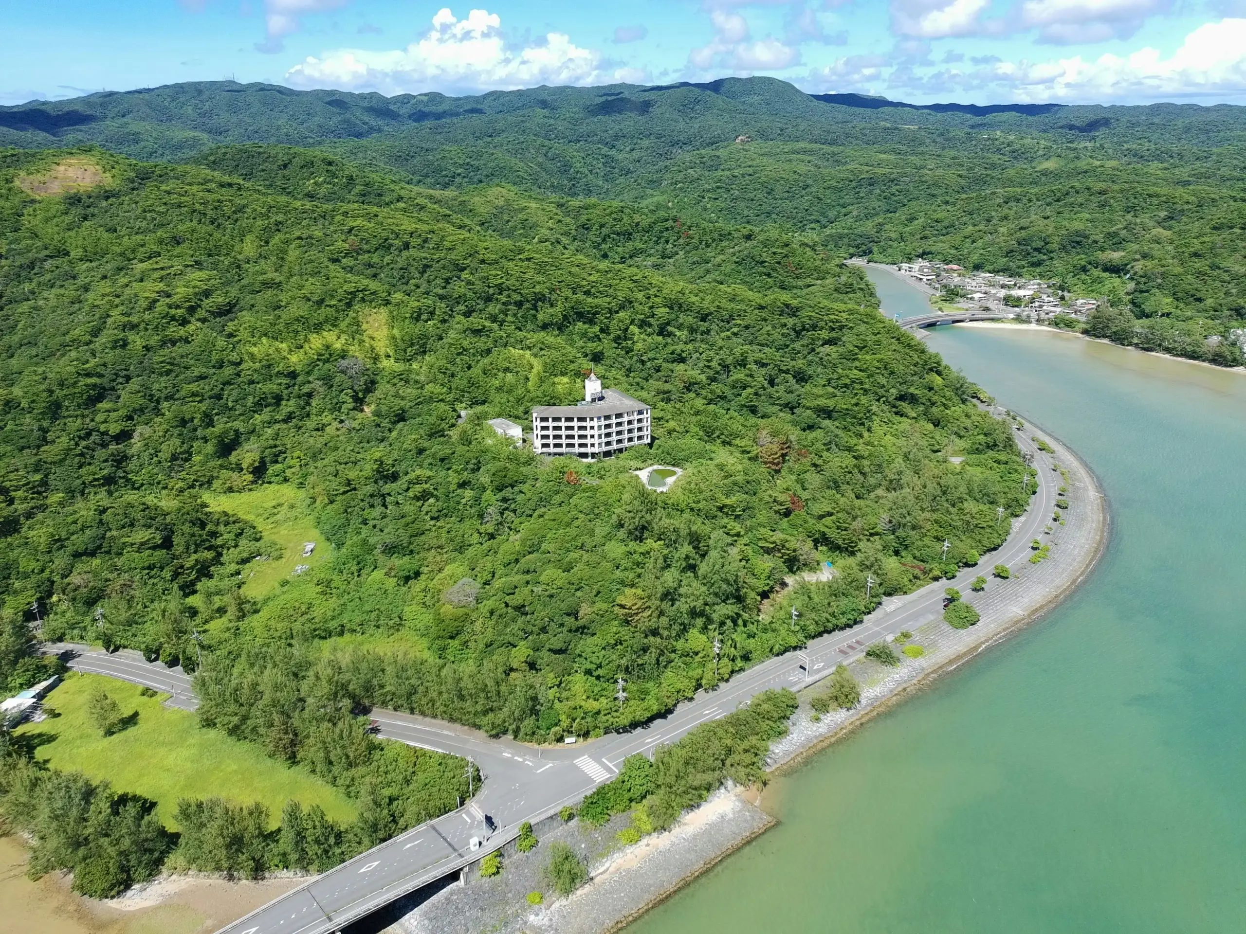 aerial view of the Sea-to-Sky Highway hugging coastline with turquoise water, steep cliffs, and cars winding through mountain curves