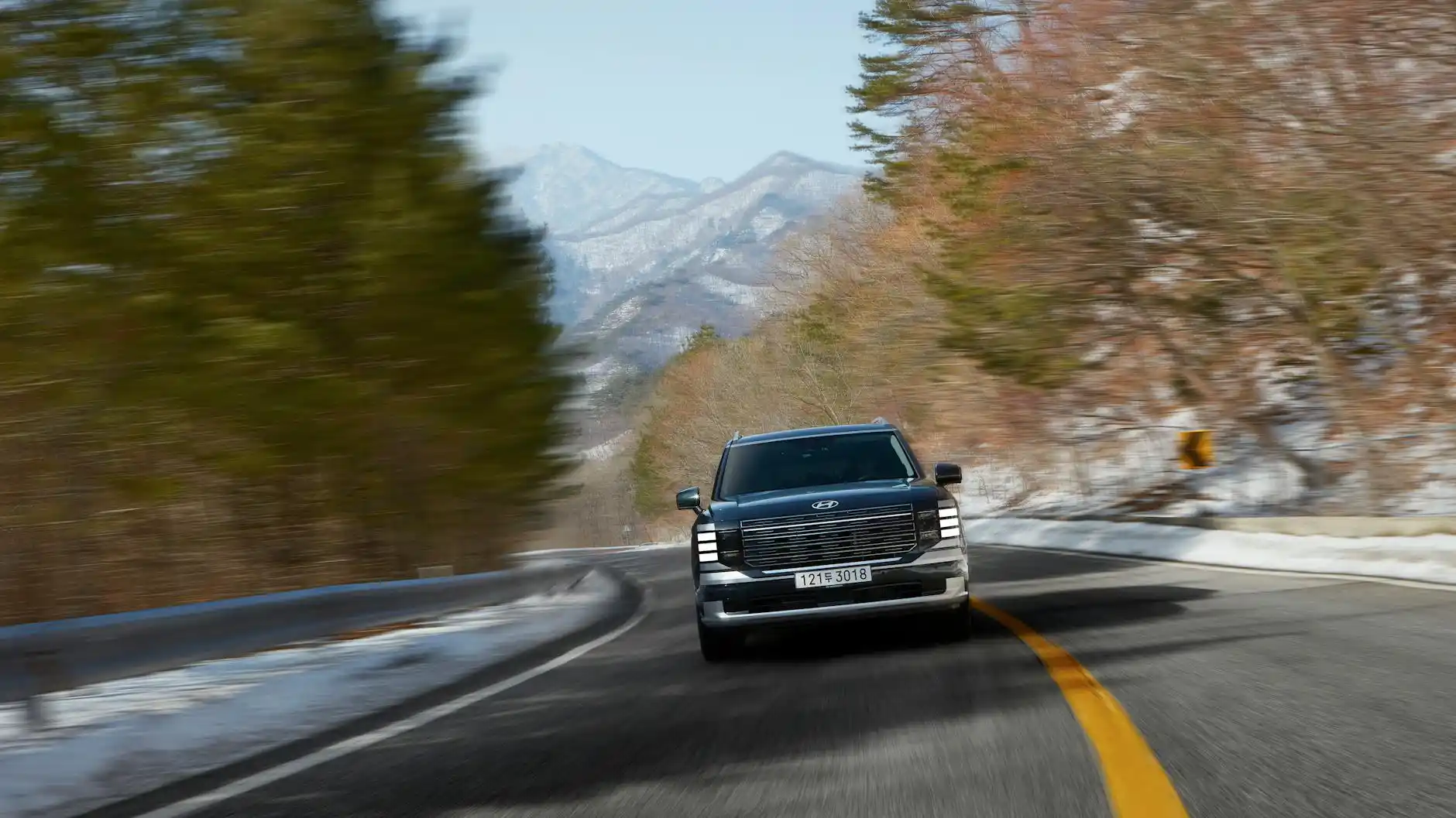 snowy mountain highway with light snowfall, SUV driving carefully with pine trees and foggy alpine backdrop