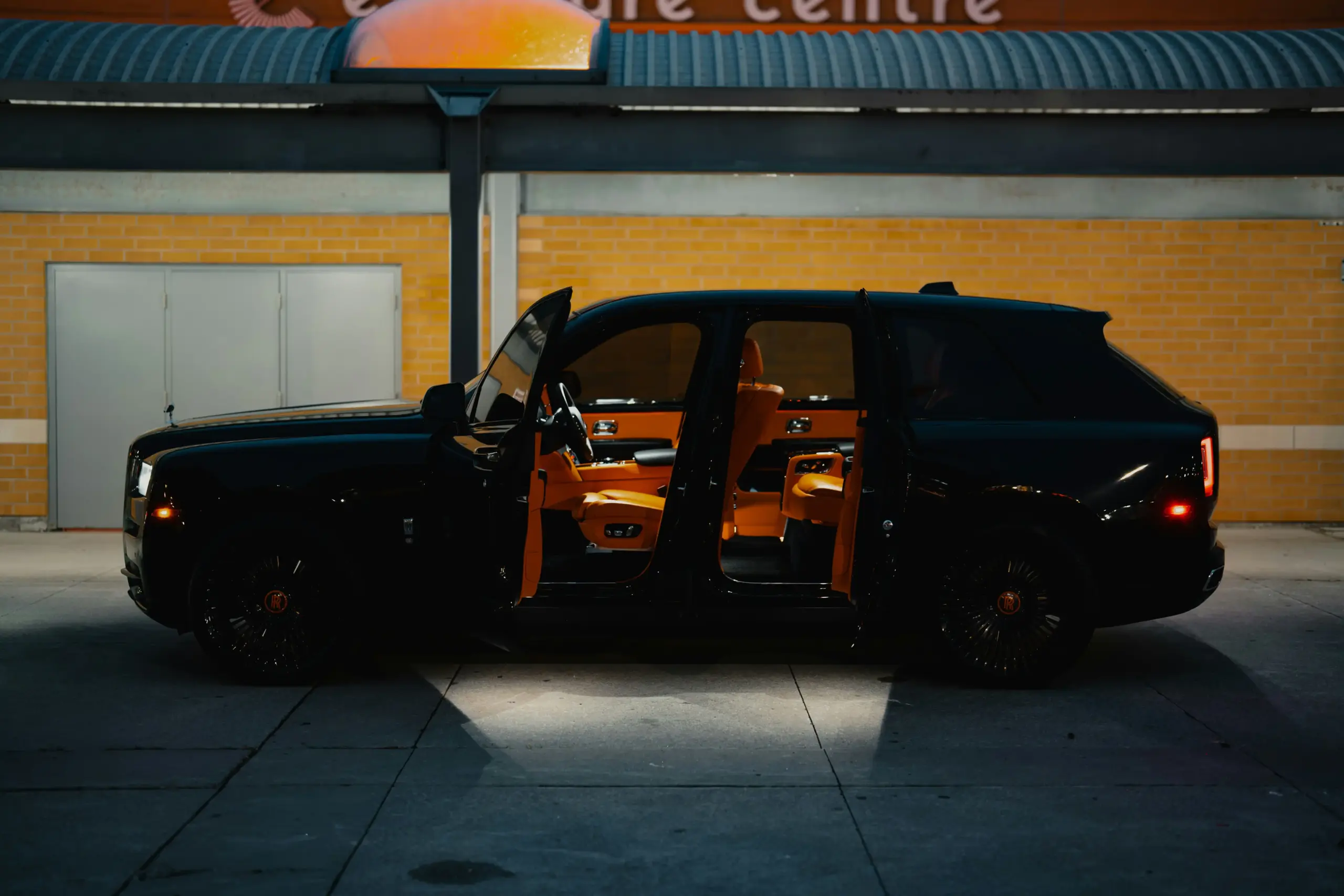 luxury black SUV parked outside a modern Woodinville winery at golden hour, guests in smart casual attire holding wine glasses near vineyard rows and tasting room entrance