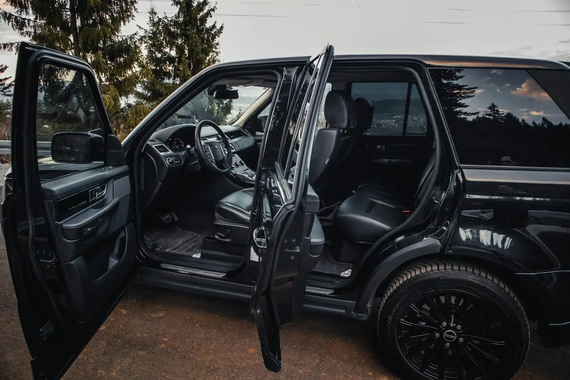 professional chauffeur opening the door of a black luxury SUV for smiling wine tour guests outside a rustic-chic Woodinville tasting room, evening light