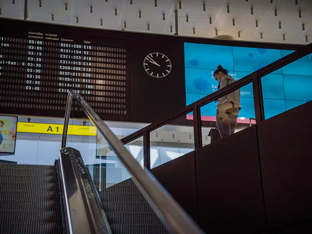 professional airport concierge in a tailored suit greeting travelers at Seattle-Tacoma International Airport arrivals hall, visible flight boards, rolling luggage, bright modern...