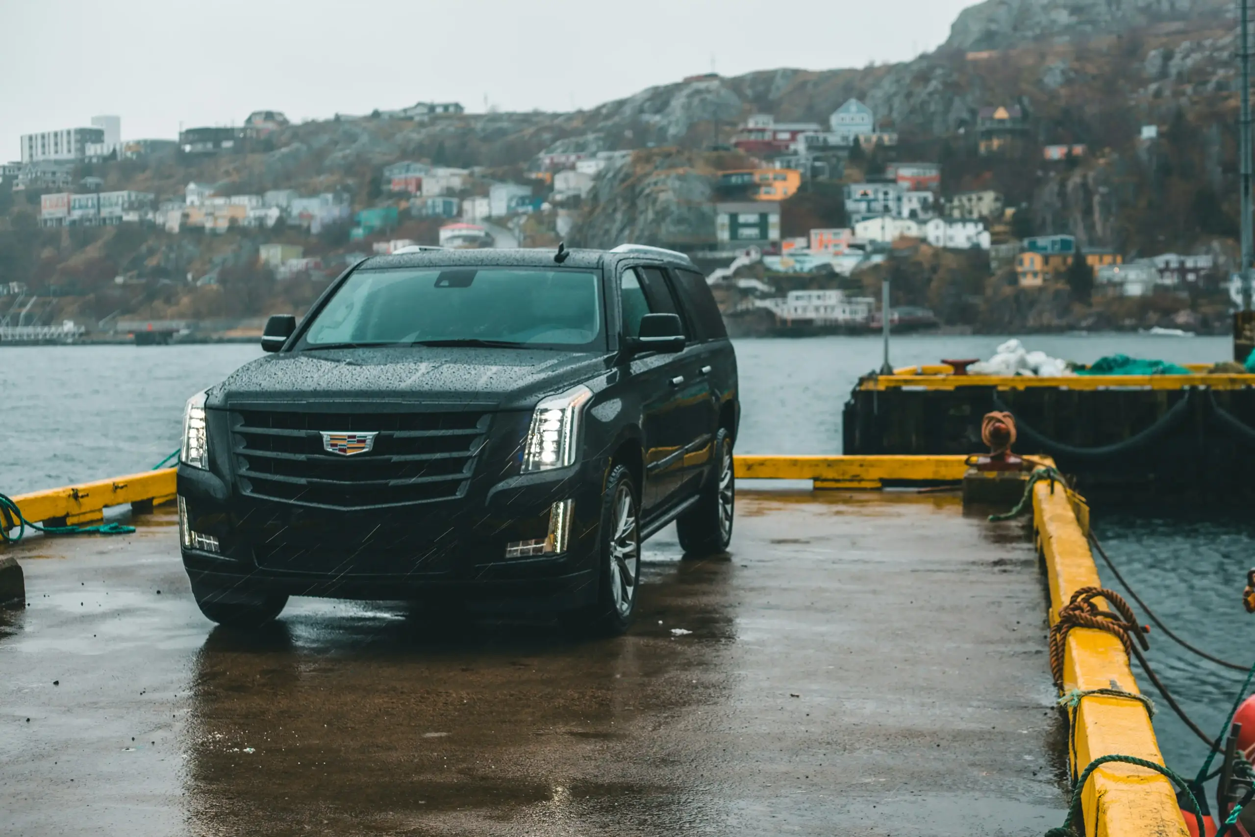 black luxury SUV parked near the Anacortes ferry terminal at sunrise, with ferries in the background, wet pavement reflecting harbor lights, Pacific Northwest coastal atmosphere
