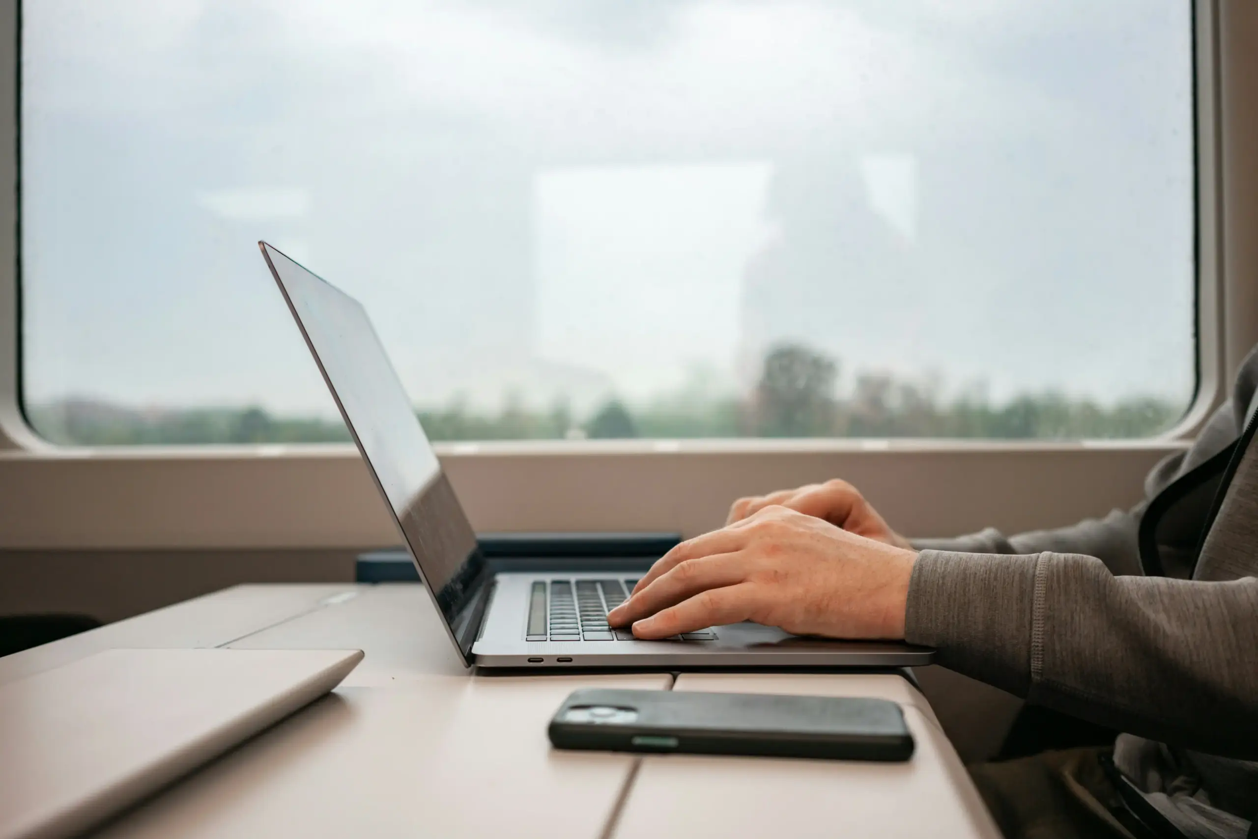 executive assistant in a modern office confirming chauffeur details on a laptop, Seattle skyline through large windows, itinerary paperwork and flight tracking screen visible on...