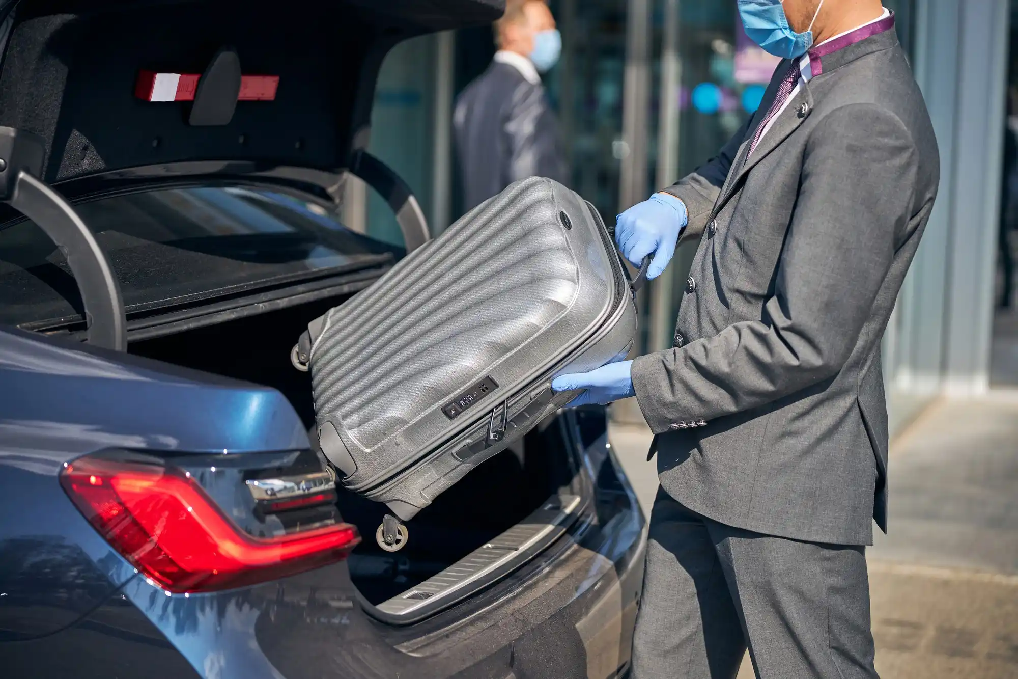 luxury black SUV parked in designated airport pickup area near SeaTac, chauffeur loading premium suitcases, rainy Seattle atmosphere with terminal lights reflecting on pavement