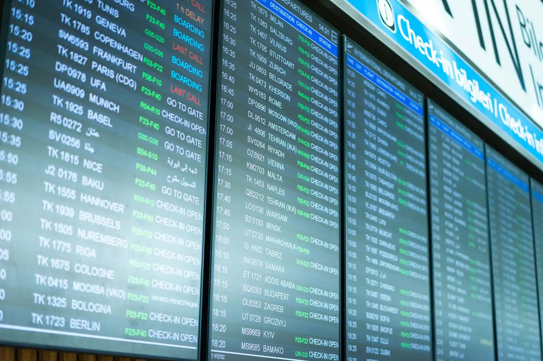 SeaTac baggage claim scene with arriving passengers, electronic flight display boards, chauffeur with tablet sign, upscale business traveler approaching with rolling suitcase