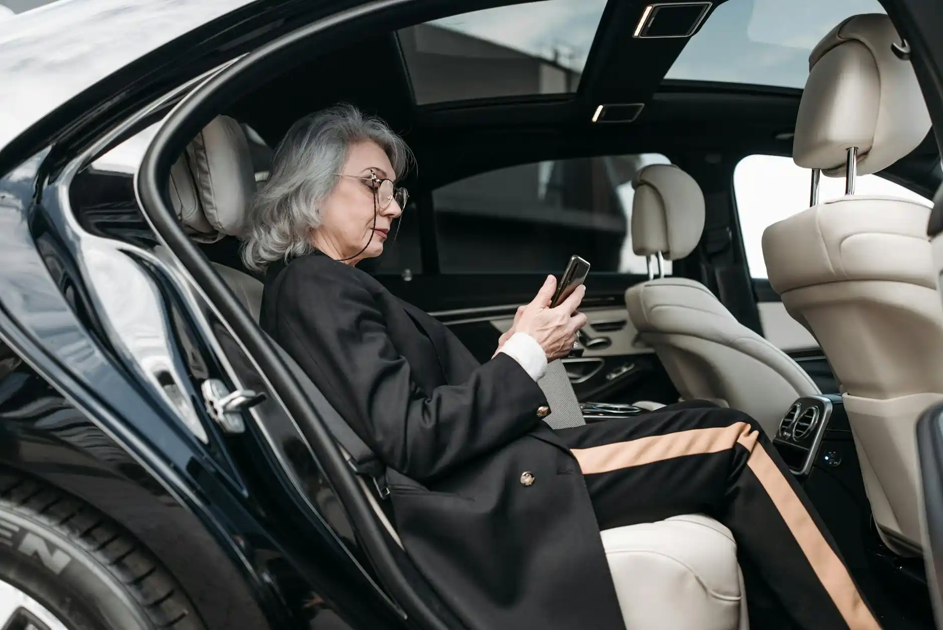 smartphone displaying live flight tracking next to a luxury car interior, chauffeur checking arrival details, rainy Seattle airport atmosphere through window