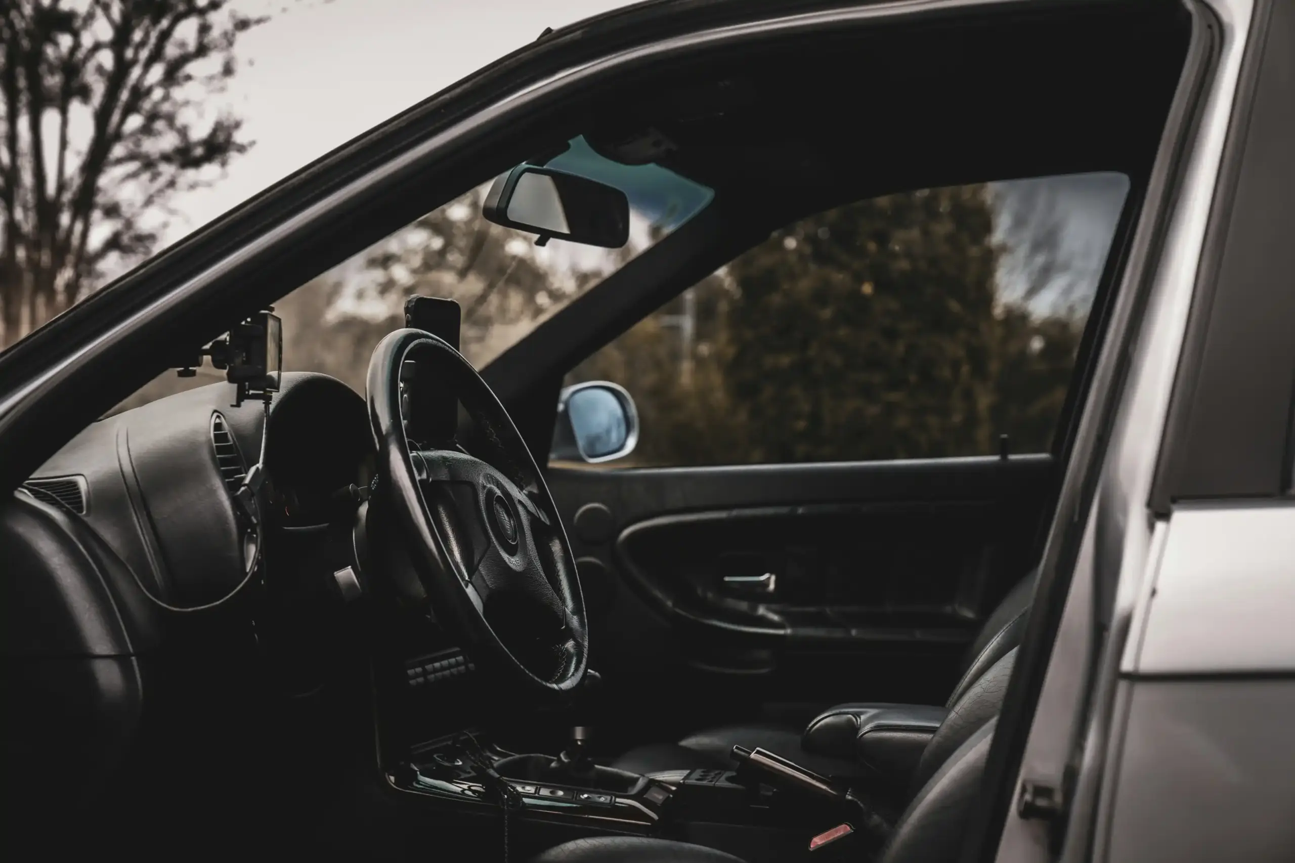 chauffeur opening rear door of executive black town car outside luxury downtown Seattle hotel, skyline in background, family with luggage and passports preparing for Vancouver t...