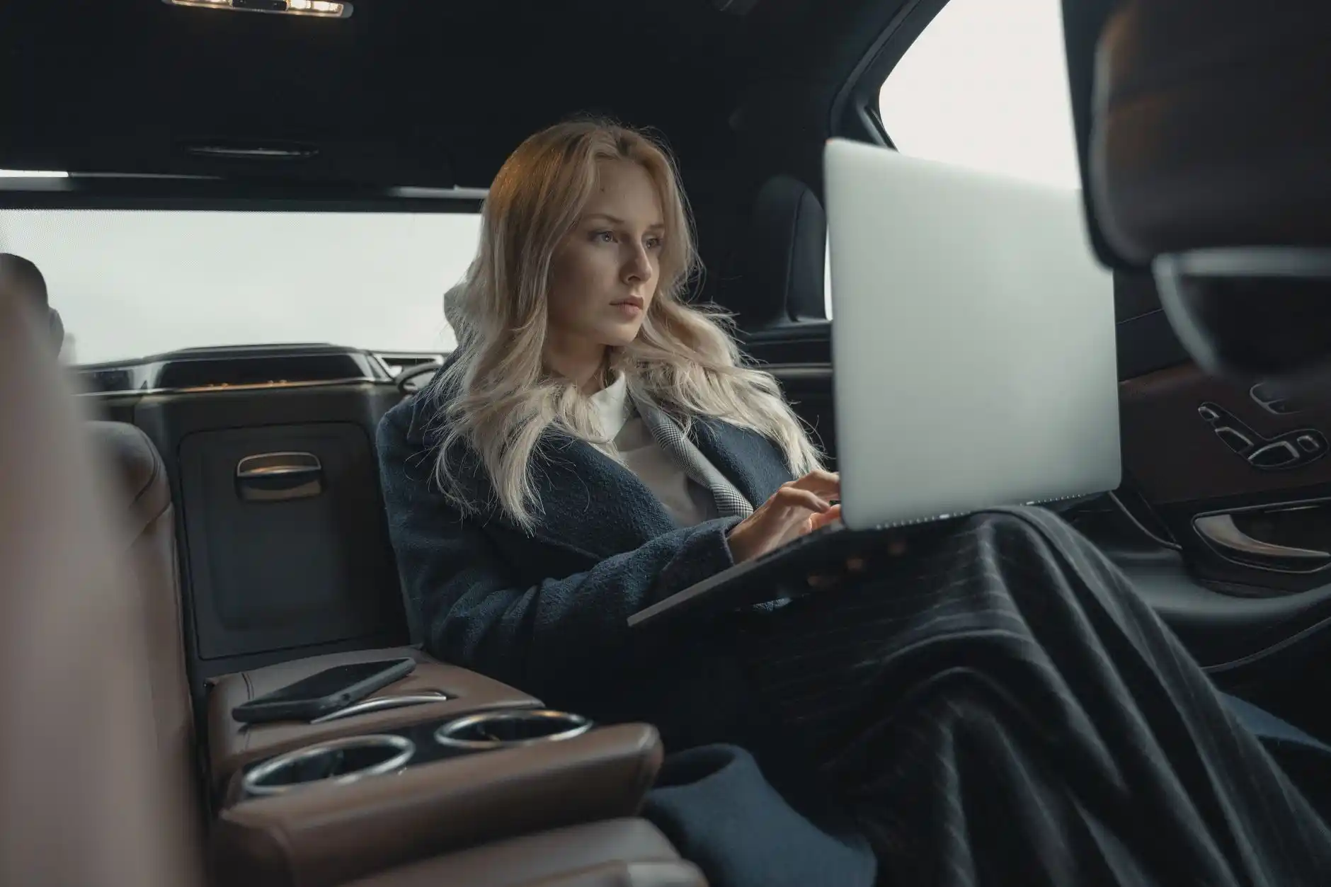 business executive in tailored suit working on laptop in back seat of luxury black sedan driving through downtown Seattle near Pike Place and waterfront at dusk