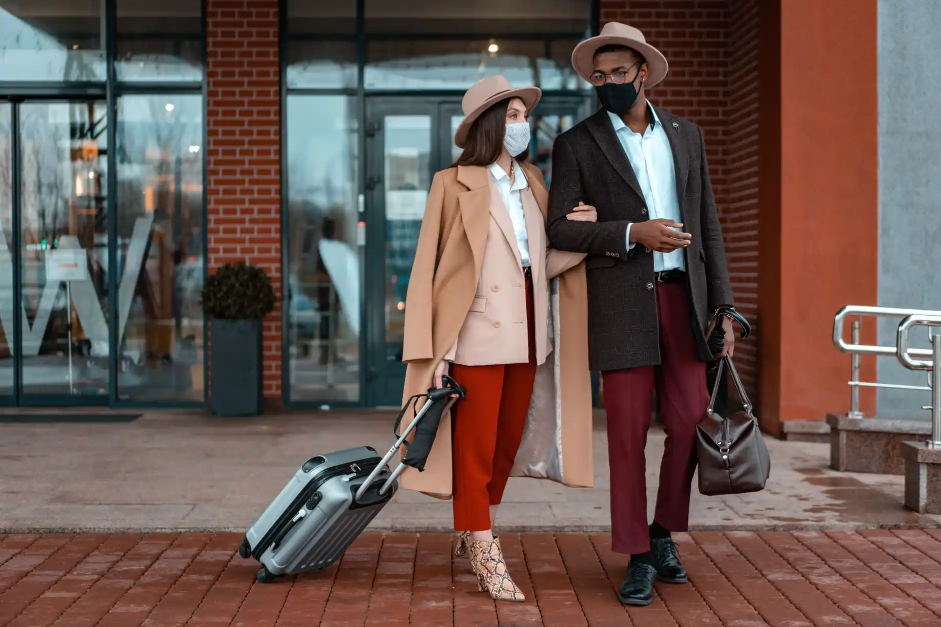 luxury sedan waiting outside an upscale Seattle hotel entrance with covered valet area, bellman nearby, couple with compact suitcases stepping out through glass doors