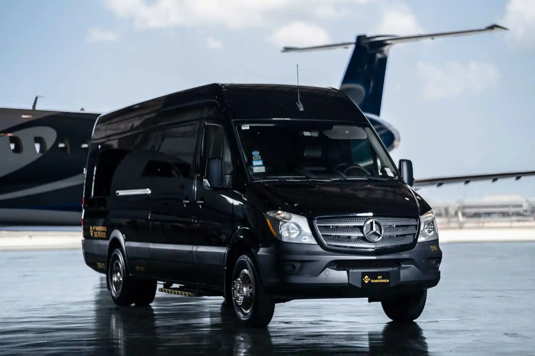 black luxury Mercedes Sprinter van parked near the Anacortes waterfront at golden hour, passengers loading luggage, marina and ferries visible in the background, Pacific Northwe...
