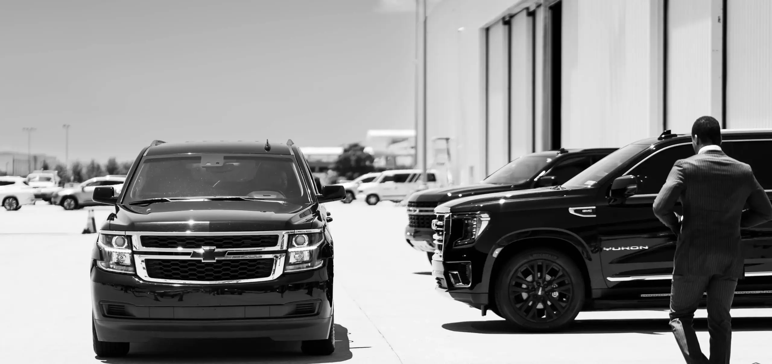 professional chauffeur loading multiple suitcases into a black luxury SUV outside an upscale Seattle hotel, early morning light, travelers in business attire preparing for airpo...