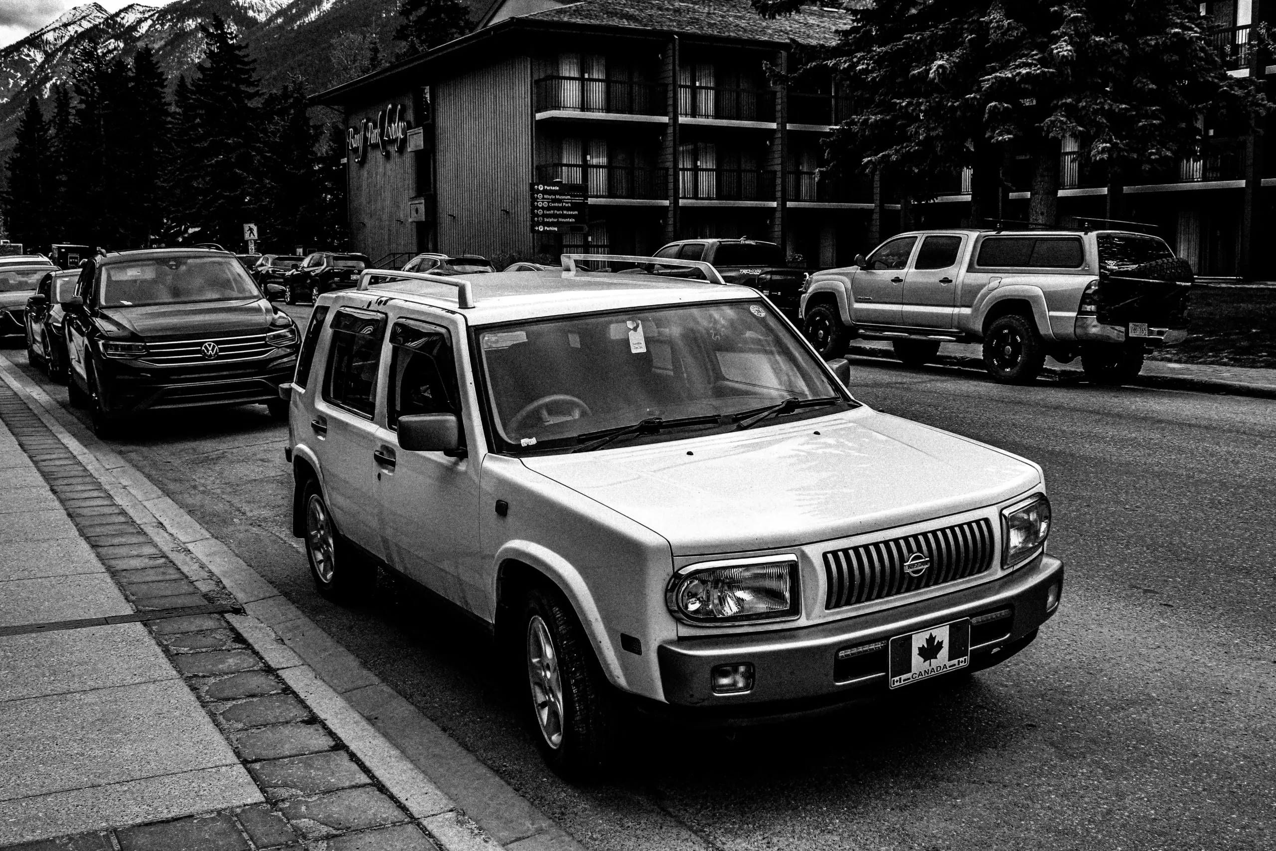black luxury SUV parked curbside outside a modern downtown Seattle hotel at dusk, chauffeur opening rear passenger door, warm lobby lighting reflecting on glossy paint, upscale ...