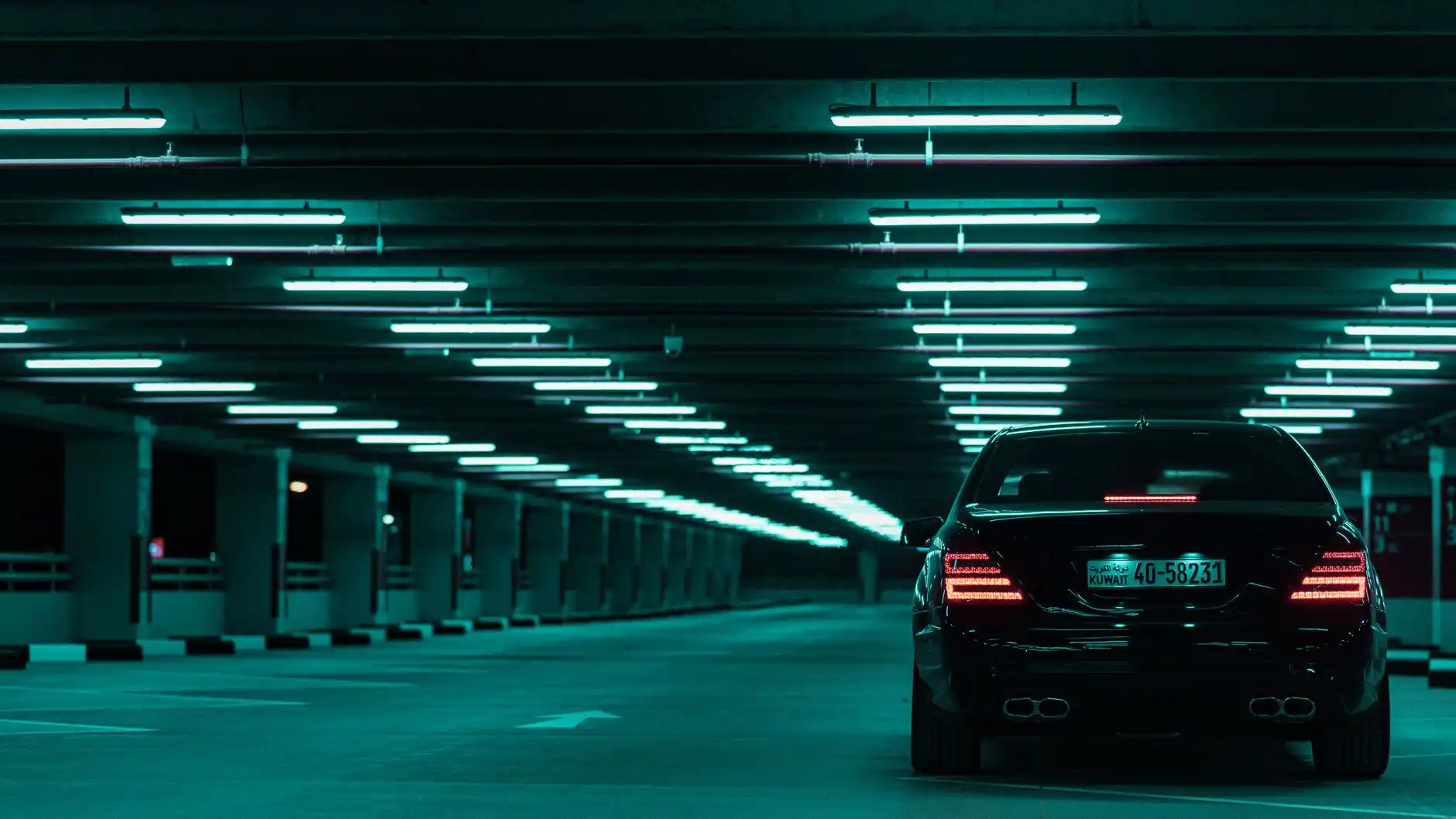 polished black town car parked in airport garage area with chauffeur in dark suit checking flight status on smartphone, ambient lighting and signage indicating terminal arrivals