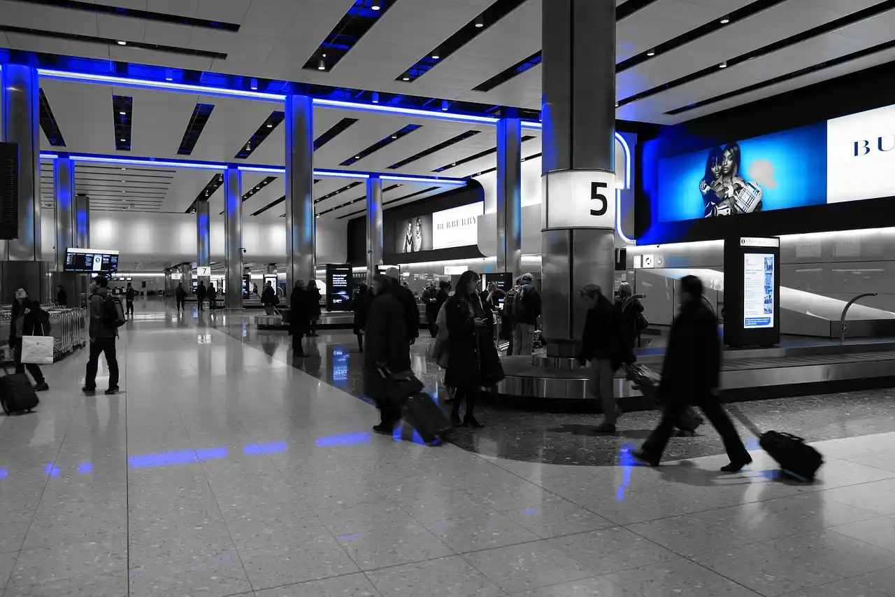 arriving passenger in Seattle airport checking smartphone next to baggage carousel while chauffeur holds a sign with passenger name, sleek terminal lighting and visible SEA wayf...