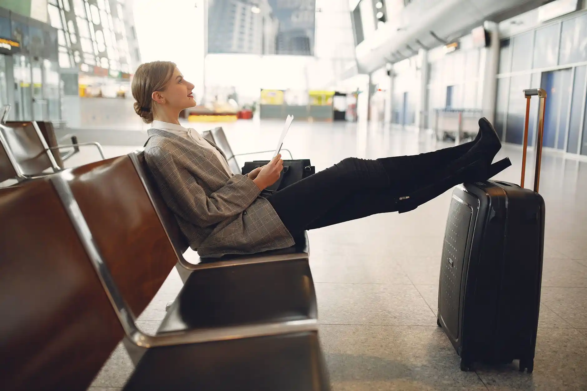 smartphone showing fluctuating rideshare prices next to printed flat-rate car service confirmation on airport terminal seating, coffee cup and boarding pass visible