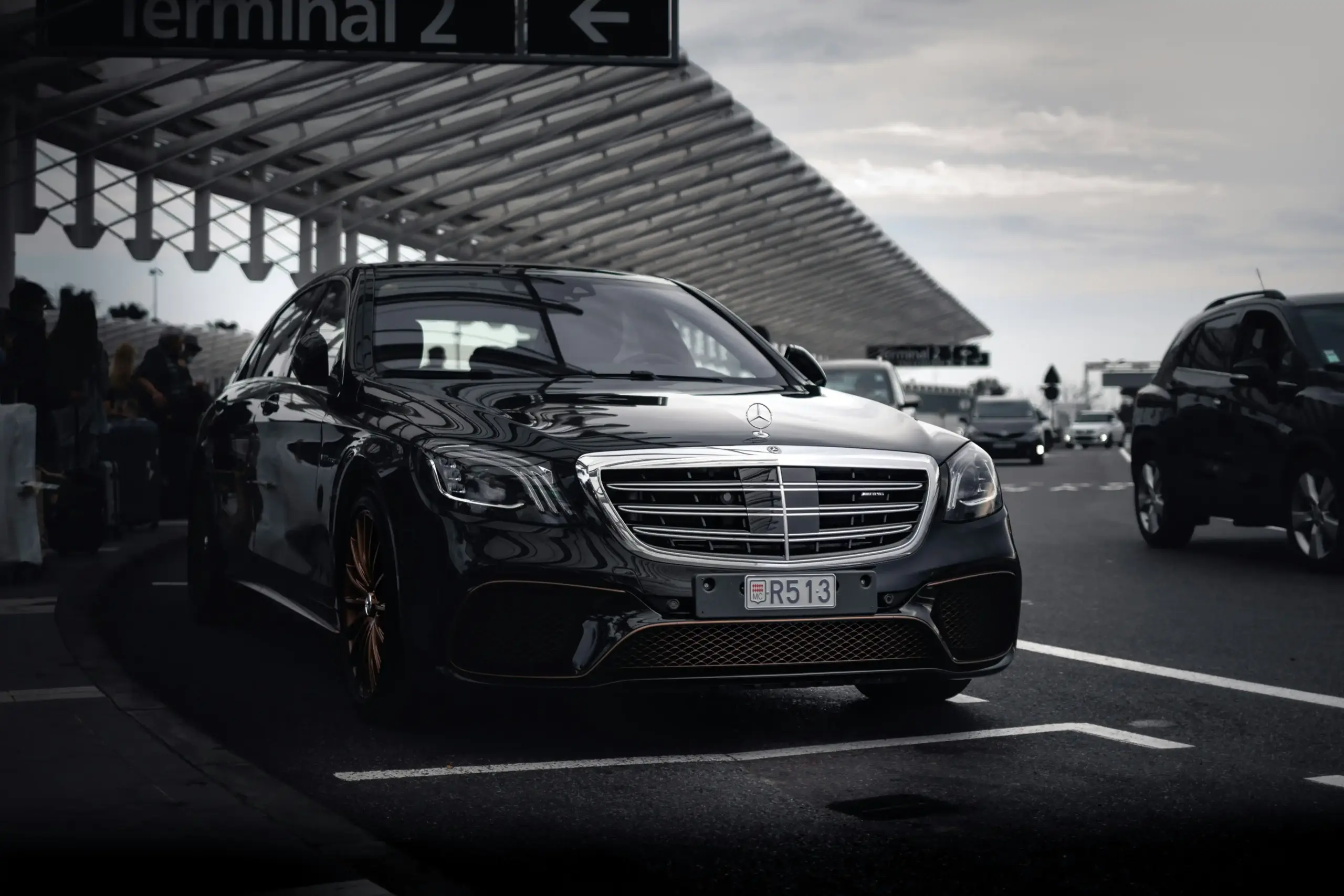 border crossing scene at Peace Arch on a clear afternoon, polished black luxury car waiting in lane, passport in hand visible from passenger perspective, evergreen trees and fla...