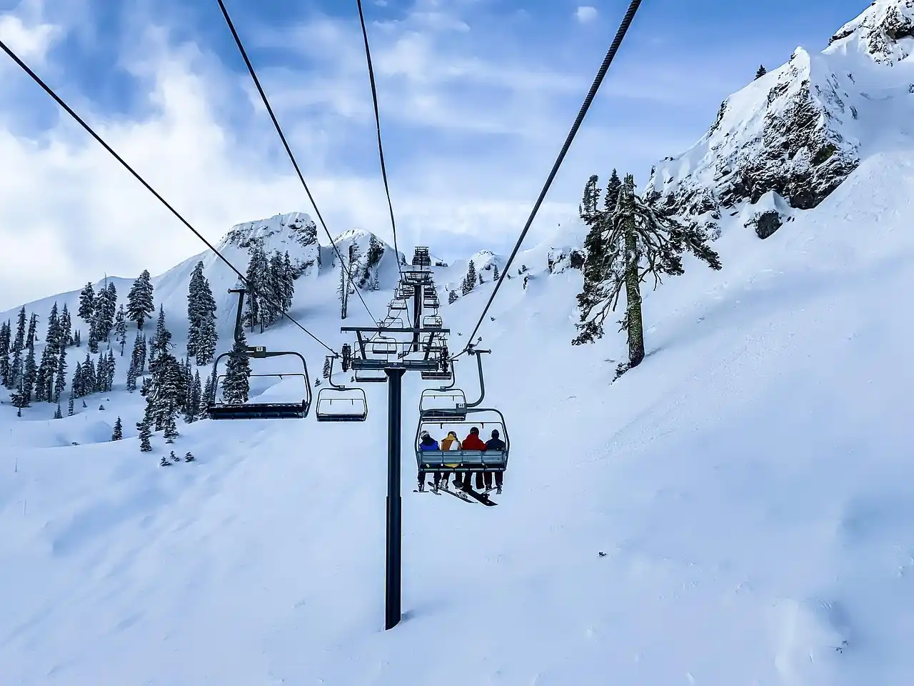 elegant mountain resort entrance in Whistler Village with snow falling lightly, guests unloading luggage and skis from a black luxury SUV