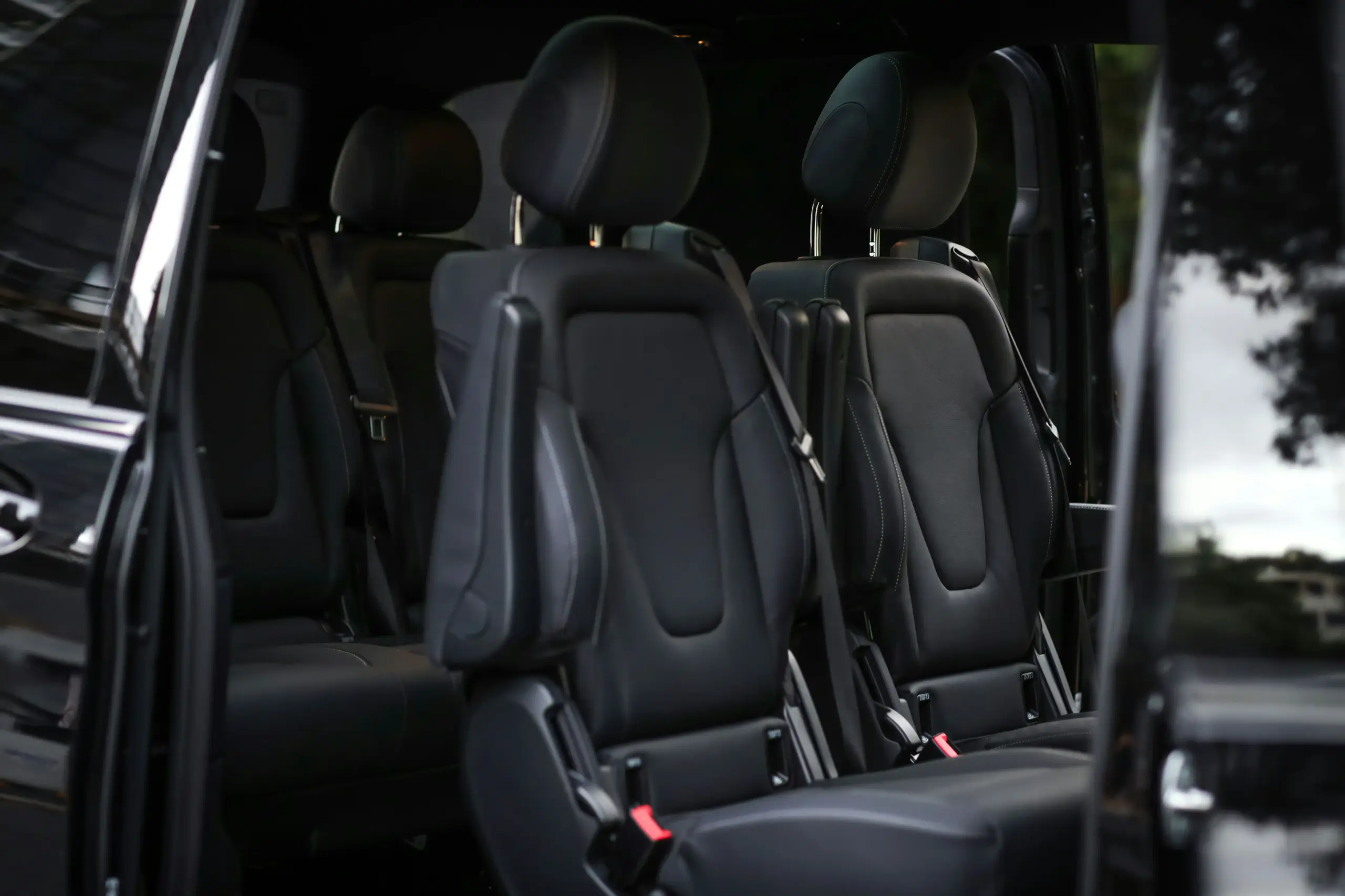 interior of a private Sprinter van with leather captain chairs, aisle access, overhead lighting, carry-on bags stored neatly, realistic upscale shuttle interior
