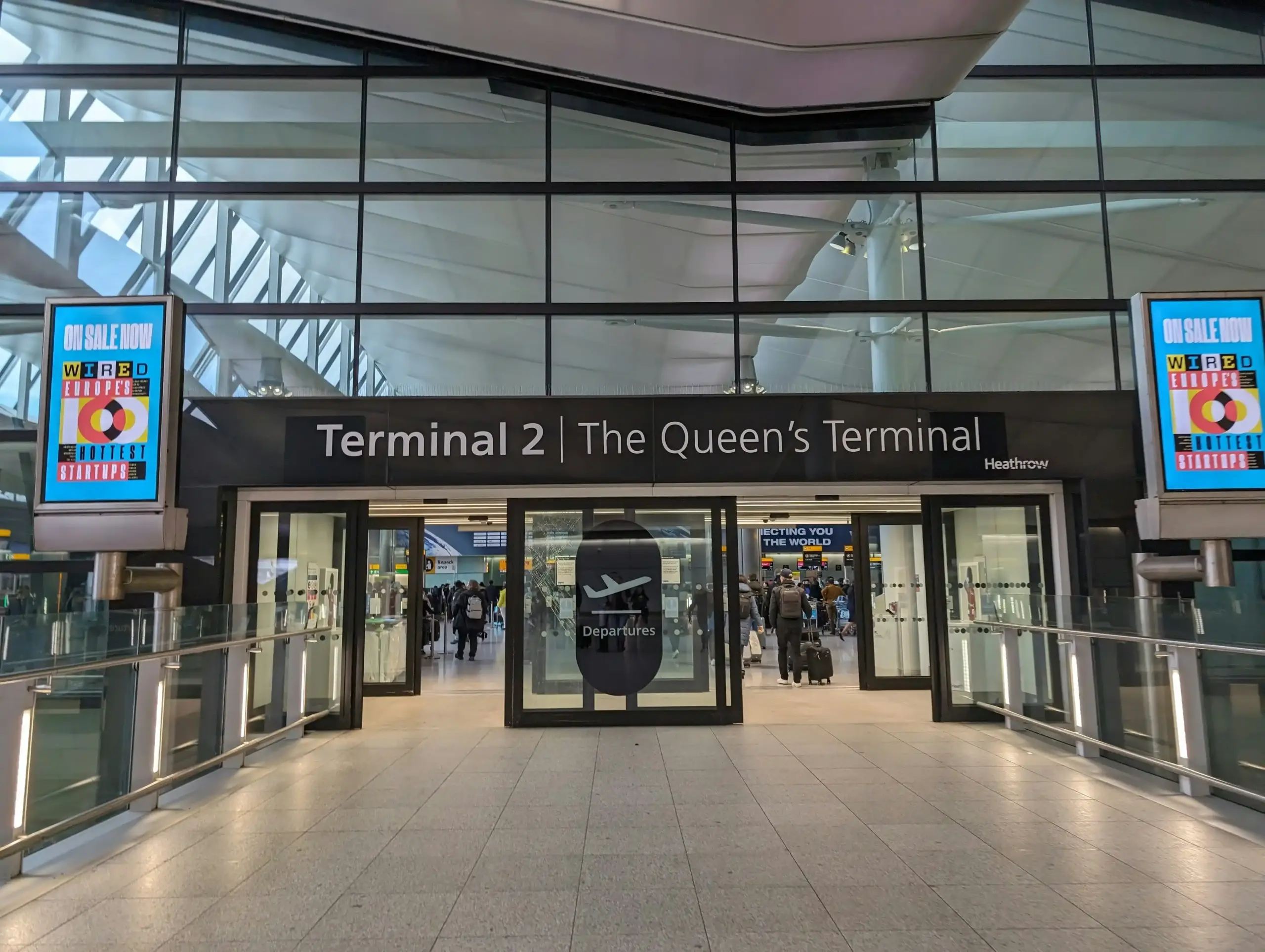 professional chauffeur in dark suit holding a name sign inside Seattle-Tacoma International Airport arrivals area, traveler with rolling luggage approaching, bright modern termi...