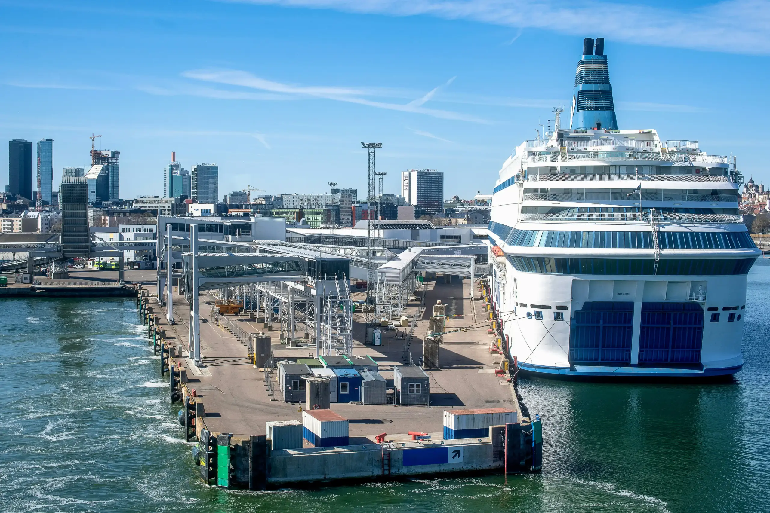 Seattle cruise terminal drop-off lane with porters, directional signs for Pier 66 and Pier 91, cars merging in organized traffic, passengers unloading suitcases
