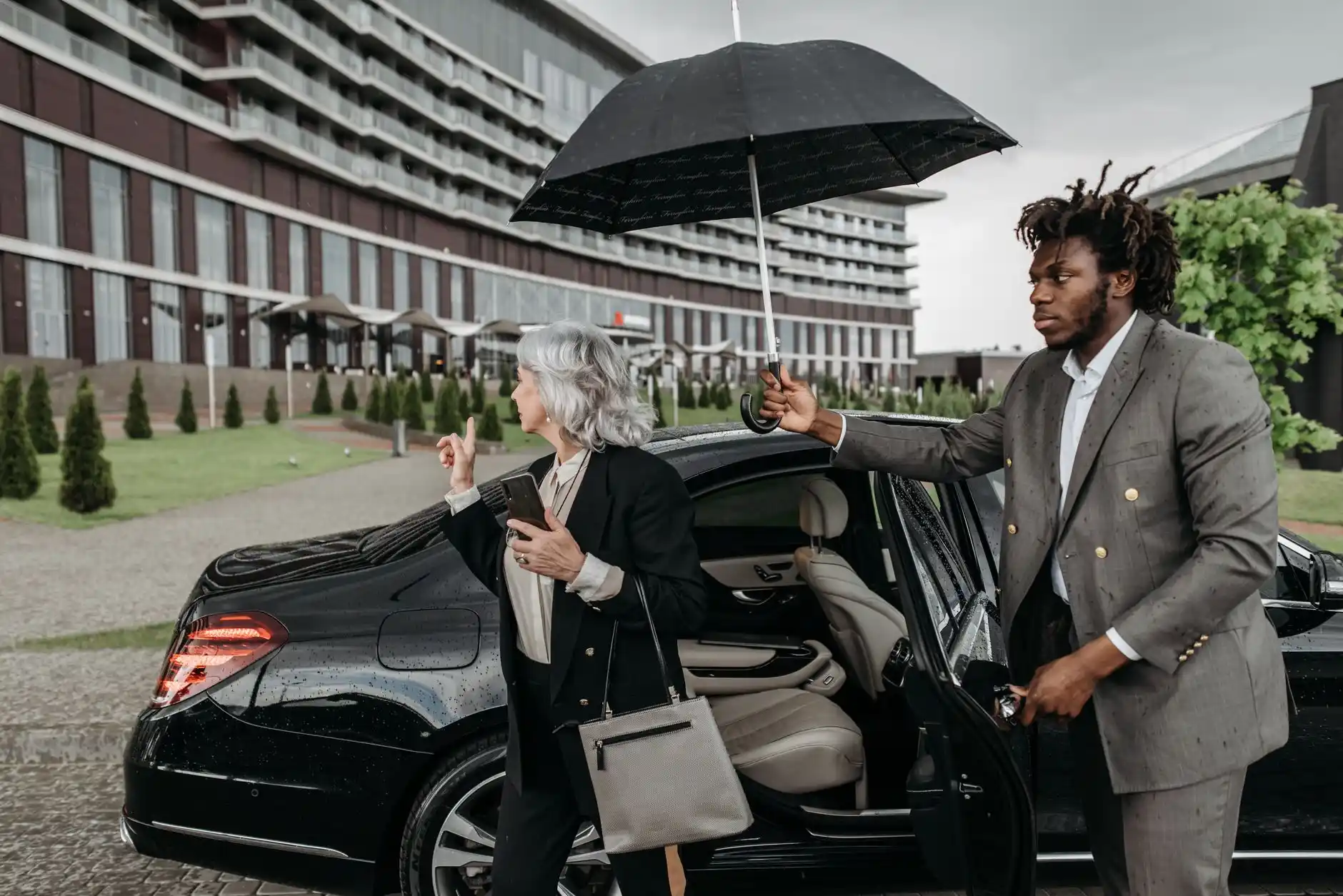 professional black SUV curbside at Seattle-Tacoma International Airport with chauffeur holding tablet, rainy Seattle evening, clean luxury travel aesthetic