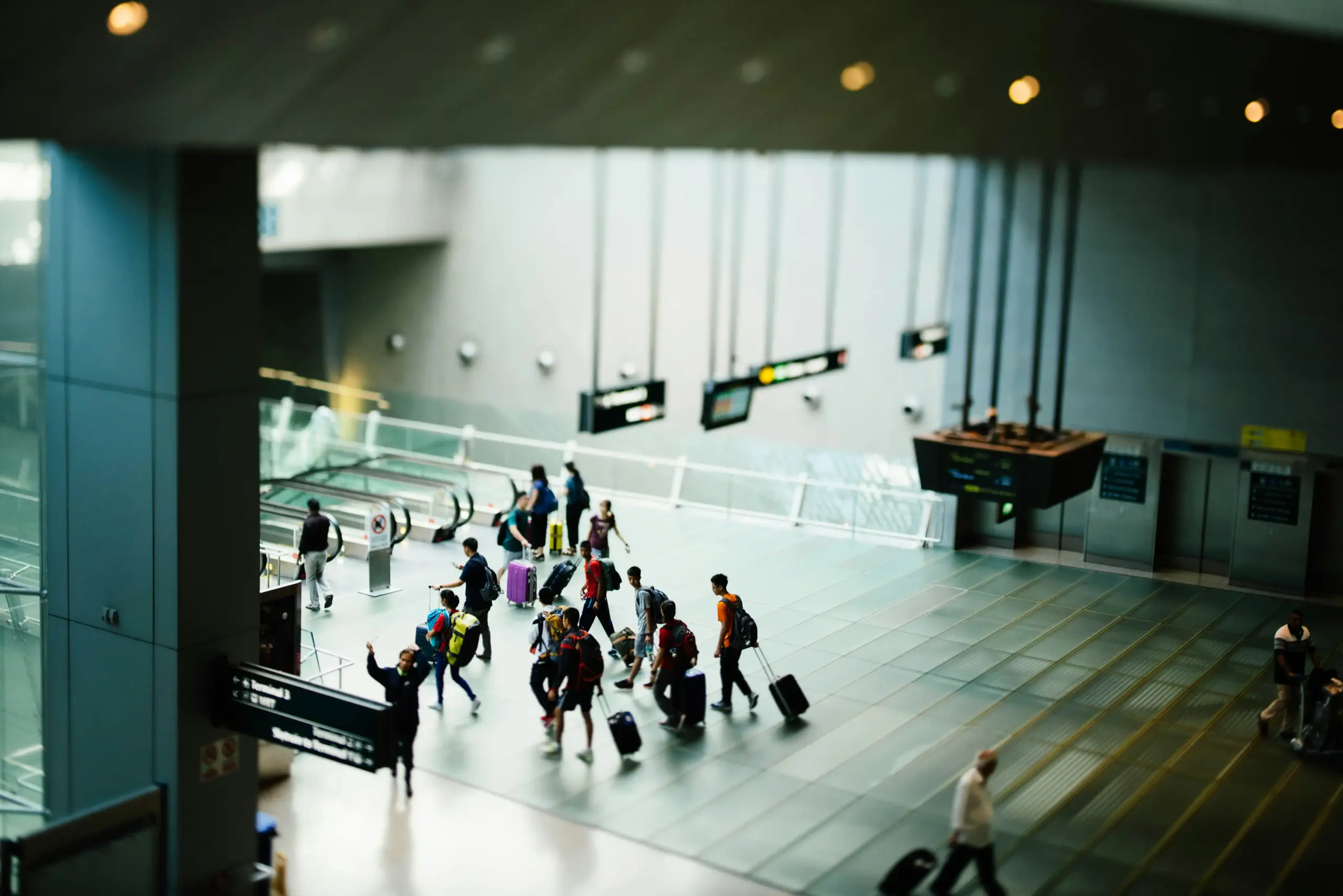 professional airport greeter in dark suit meeting travelers with rolling luggage inside Seattle Tacoma International Airport, clear terminal signage, premium business travel atm...