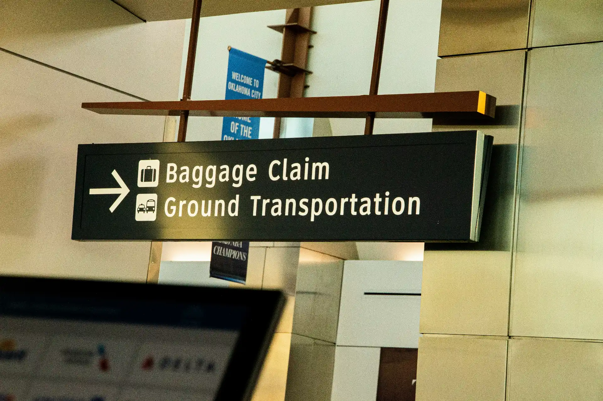 Professional chauffeur holding a passenger name sign inside Seattle-Tacoma International Airport baggage claim, with luggage carousels and clear terminal signage in the background