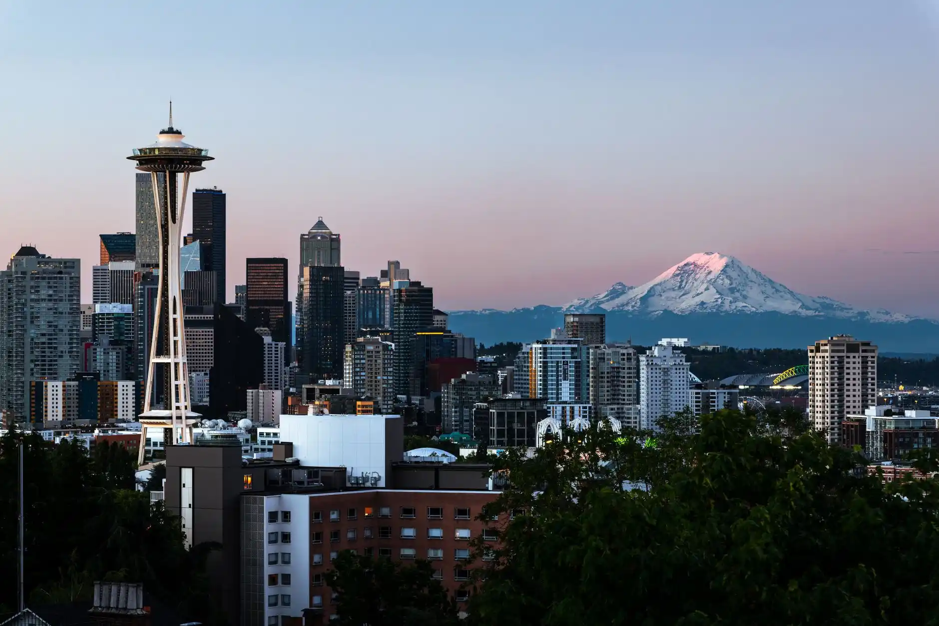 luxury vehicle overlooking Kerry Park view of Seattle skyline at sunset, passengers taking photos, Space Needle and Mount Rainier visible in dramatic light