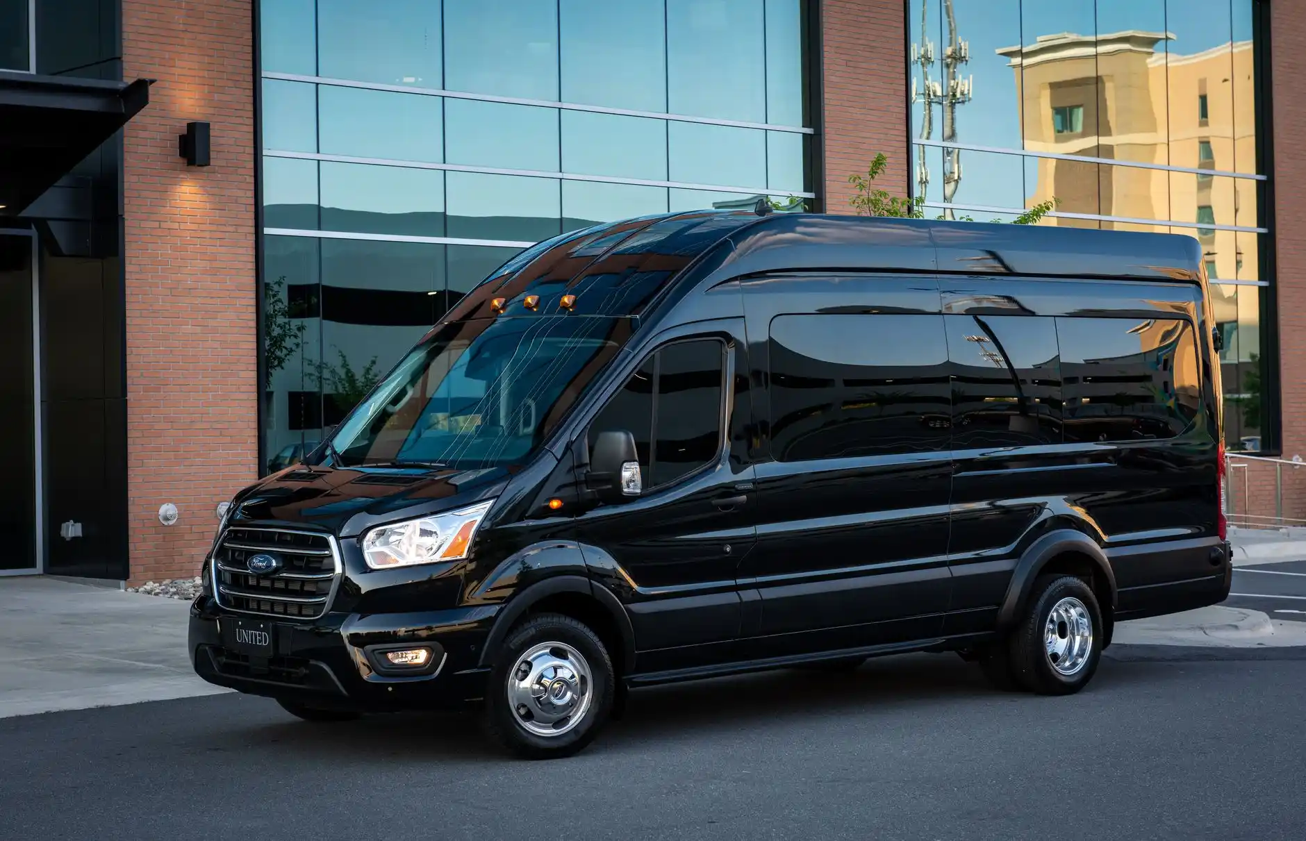Private black passenger van overlooking orderly Pacific Northwest vineyard rows, evergreen hills in the distance, clear late-morning light
