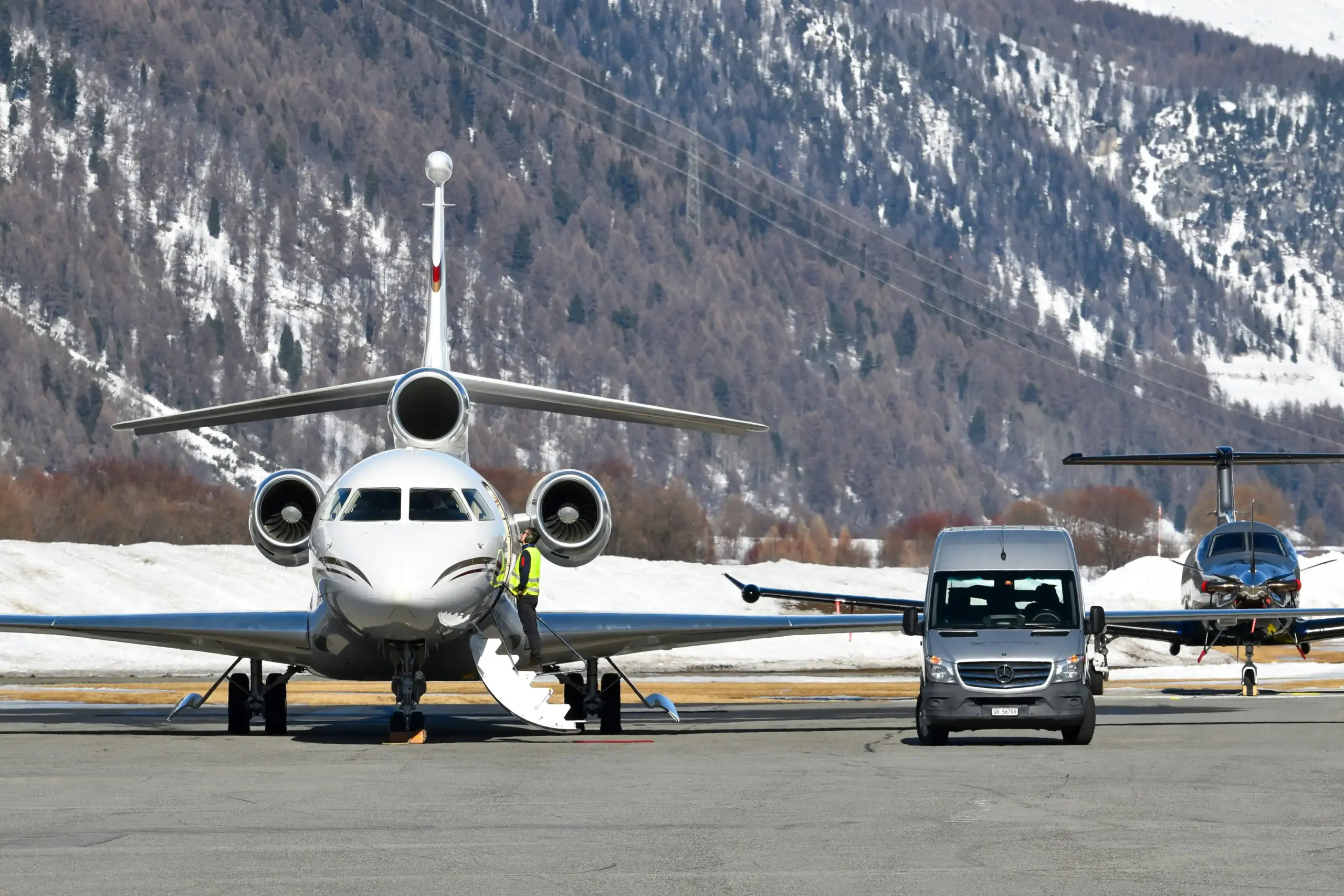 black luxury SUV positioned on an airport tarmac beside a private jet at a Seattle-area FBO, chauffeur in dark suit handling luggage discreetly, overcast Northwest light