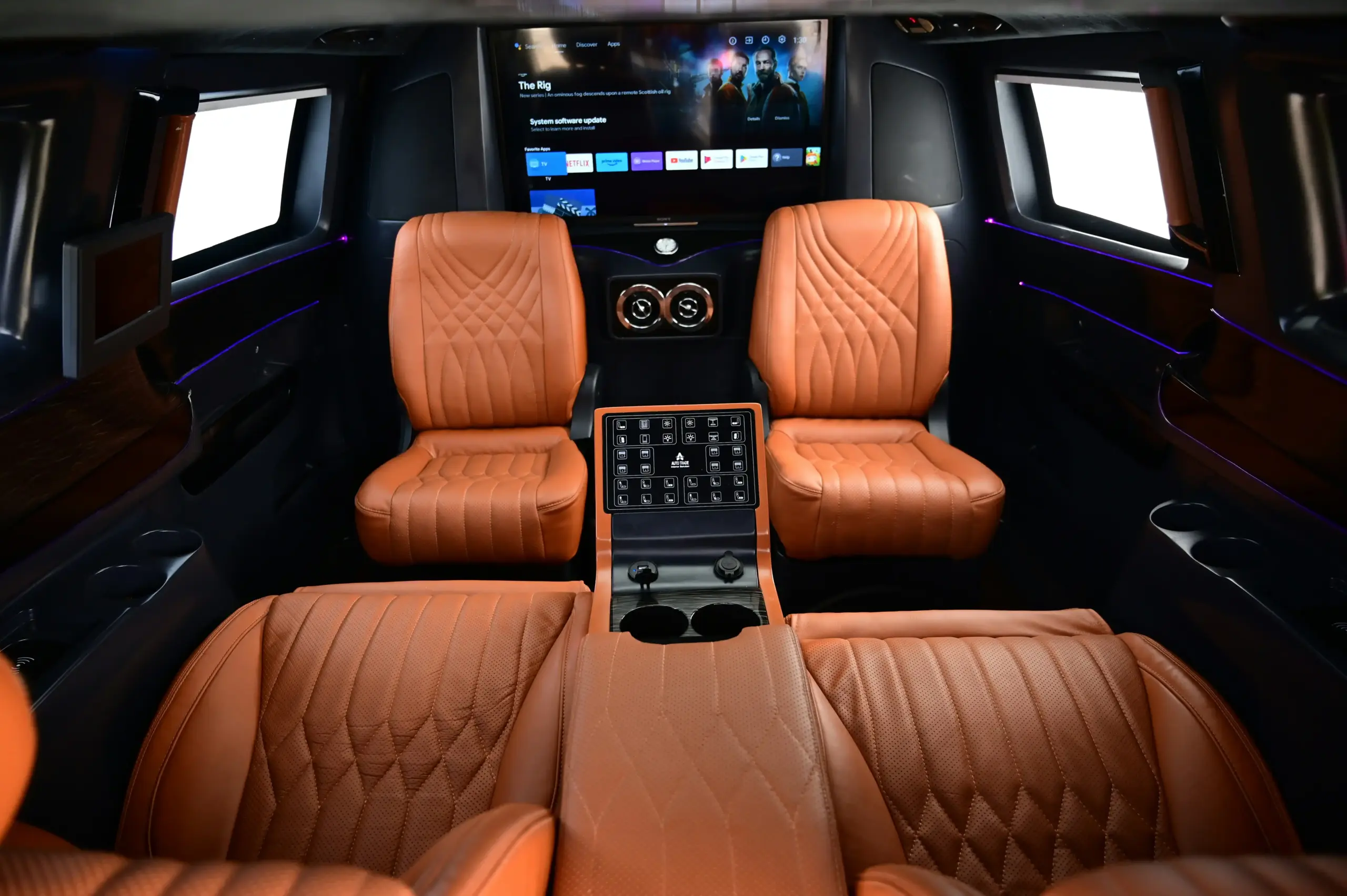 interior of a premium executive SUV with tan leather seating, rear climate controls, bottled water, charging ports, and soft ambient lighting