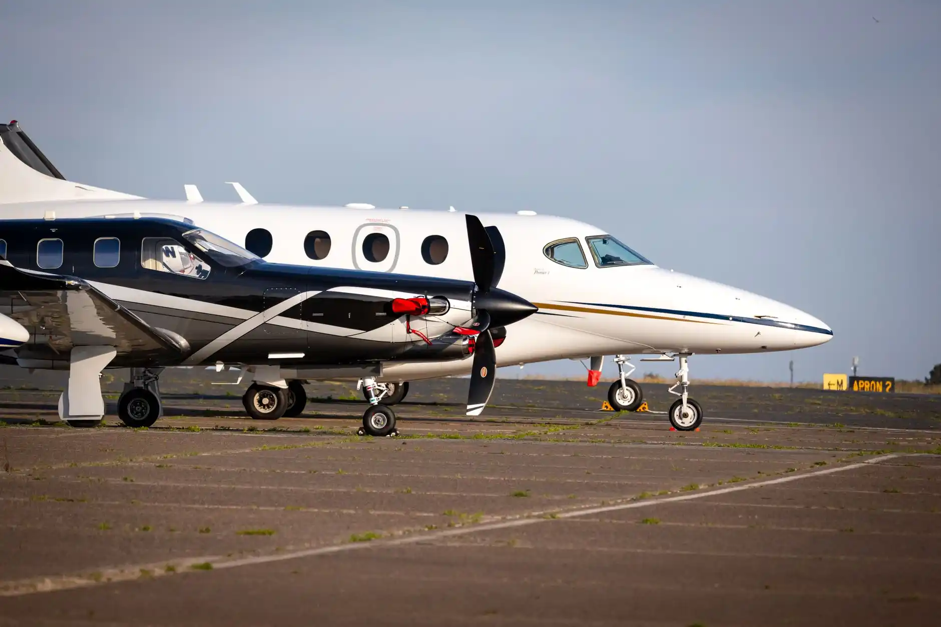 Black luxury SUV waiting outside a private aviation terminal at Boeing Field in Seattle, chauffeur standing beside the rear door, business jet visible on the ramp